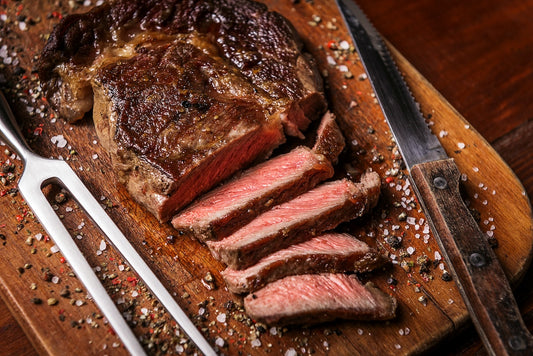 Sliced steak on a wooden cutting board with a knife and fork, surrounded by spices.