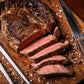 Sliced steak on a wooden cutting board with a knife and fork, surrounded by spices.