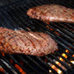 Two steaks cooking on a grill with flames below