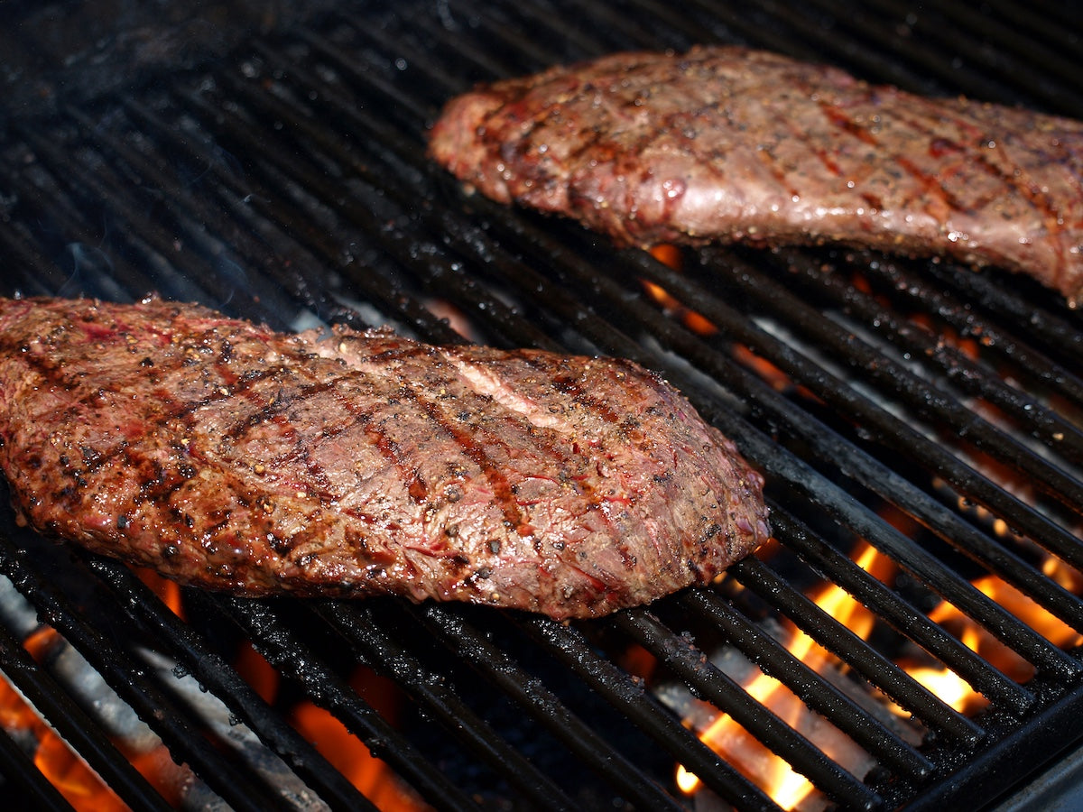 Two steaks cooking on a grill with flames below