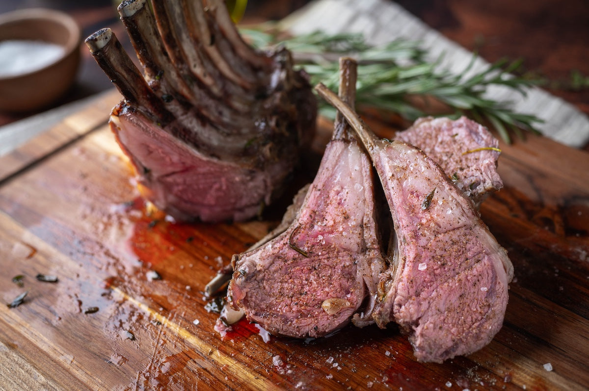 Roasted lamb chops on a wooden cutting board with herbs