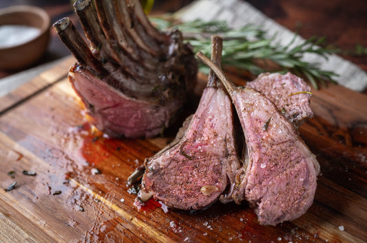 Roasted lamb chops on a wooden cutting board with herbs